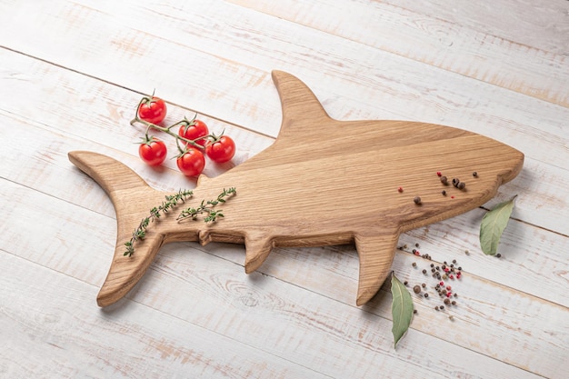 Planche à découper en bois en forme de poisson ou de requin avec tomates cerises et épices sur une maquette de fond blanc avec espace de copie pour la vue latérale du texte