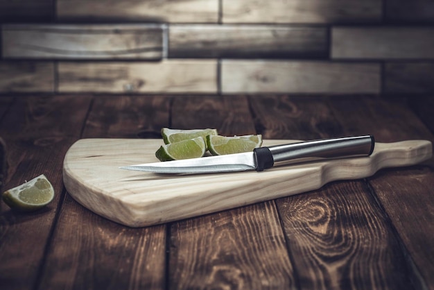 Planche à découper en bois léger avec un couteau et des morceaux de citron vert sur une table en bois