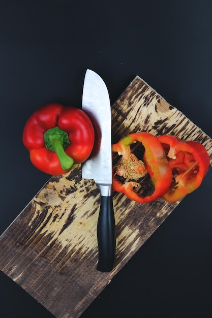 Planche à découper en bois avec poivre de légumes crus sur planche à découper rustique Poivre en tranches et couteau avec manche en bois sur planche à découper rustique