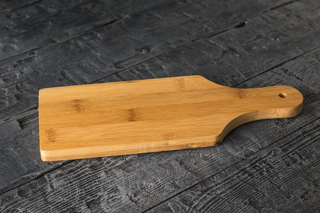 Planche à découper en bois sur table en bois noire. Accessoires de cuisine.