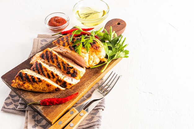 Une planche à découper en bois avec des tranches de délicieux tombeau de poulet grillé juteux coupé dessus sauce tomate dans un bol espace de fond blanc pour le texte