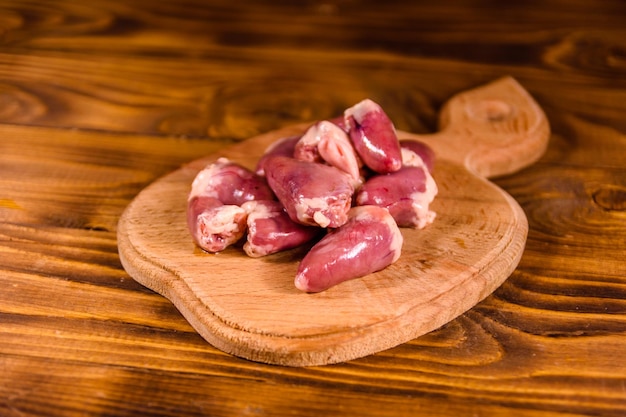 Planche à découper avec des coeurs de poulet cru sur table en bois