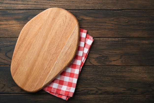 Planche à découper avec cuillères de cuisine et serviette rouge et tomate de persil pour la cuisson sur fond sombre en bois ancien Santé alimentaire végétarienne ou concept de cuisine Fond de nourriture avec espace libre pour le texte