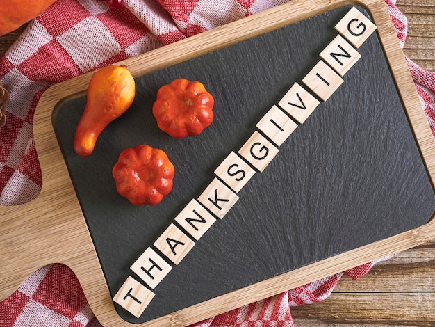 Planche à découper avec l'inscription de cubes en bois Thanksgiving une serviette de cuisine dans un cadre rouge et des citrouilles se trouvent sur une table en bois vue de dessus dans un gros plan à carreaux