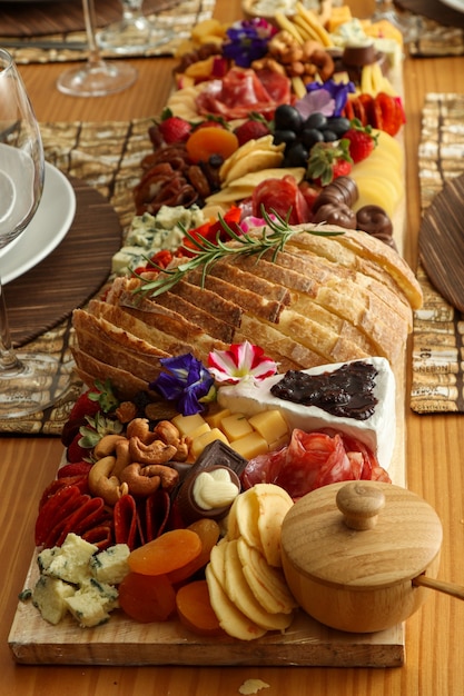 Photo planche à découper en marbre avec mousse de gorgonzola, brie, pain, chocolat, confiture, raisins, fruits, noix, fleurs comestibles, salame, etc.