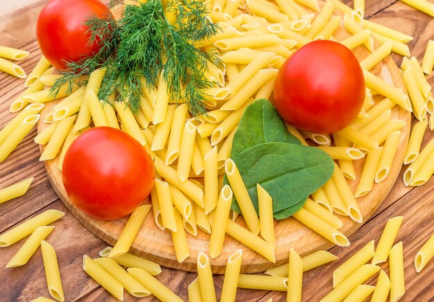 Planche à découper avec pâtes crues tomates épinards et aneth sur table en bois