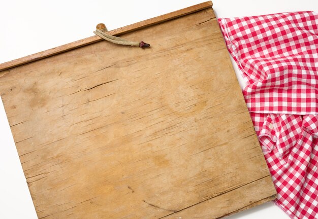 Planche à découper rectangulaire vide de cuisine en bois et serviette rouge dans une cage blanche sur une table blanche, vue de dessus