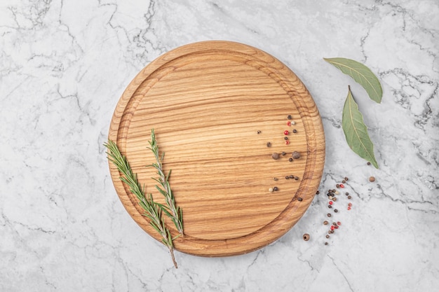 Planche à découper ronde en bois avec bordure thym et épices sur une maquette de fond en marbre blanc avec espace de copie pour la vue de dessus de texte