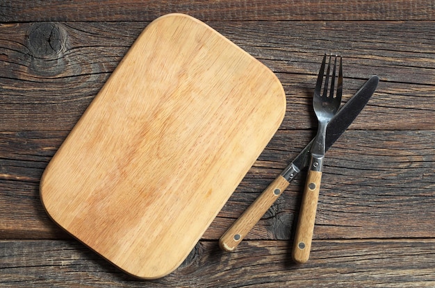 Planche à découper vide et couverts sur une vieille surface en bois, vue de dessus. Fond de nourriture