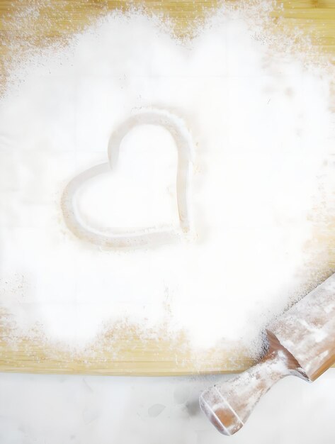 une planche avec de la farine et un rouleau à pâtisserie dessinant un coeur dessus