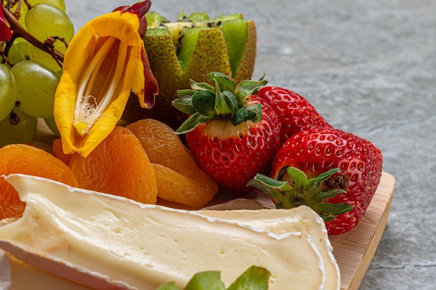 Planche de froid et de fruits servis sur fond de bois et marbre avec jambon fromage fraises salami brun...