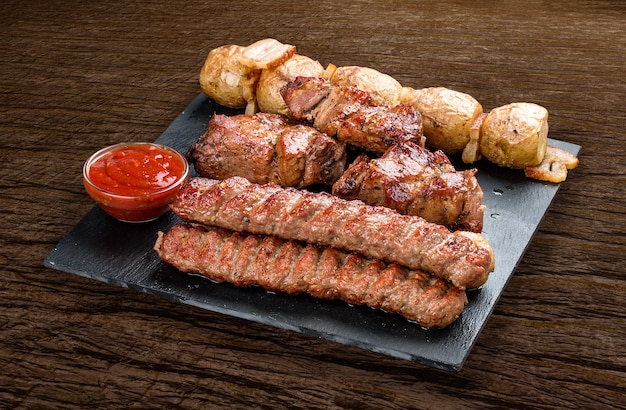 Planche de pierre avec différentes viandes cuites savoureuses sur fond de bois Pommes de terre lyulya kebab de porc