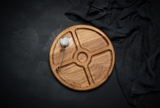 Planche ronde en bois pour servir de la nourriture et un tamis avec du sucre sur une vue de dessus de table noire