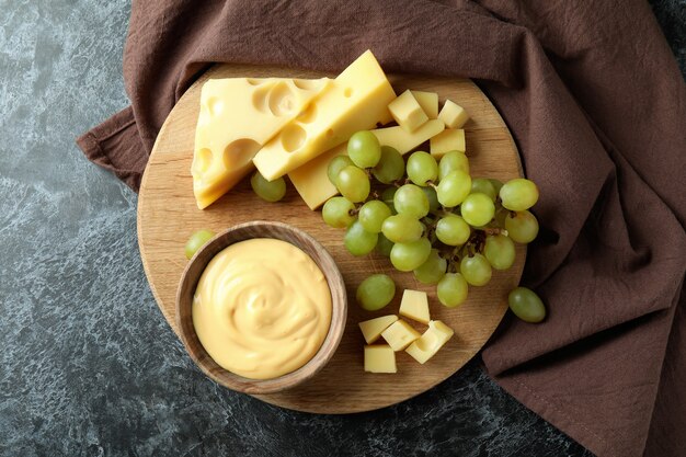 Planche avec sauce au fromage, raisin et fromage sur une table fumée noire avec un torchon