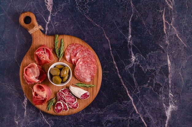 Planche de service avec un ensemble de différentes collations à base de viande, vue de dessus.