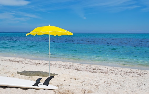 Planche de surf blanche et parasol jaune sur le sable