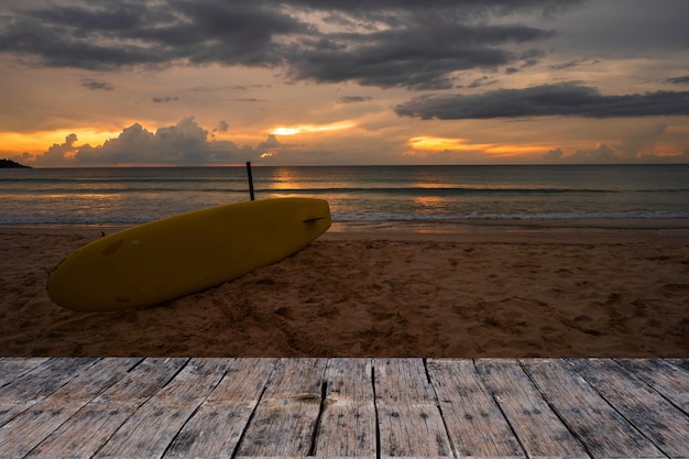 Une planche de surf jaune se trouve sur une terrasse en bois surplombant l'océan.