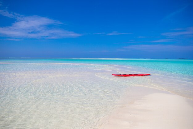 Planche de surf rouge sur une plage de sable blanc aux eaux turquoises