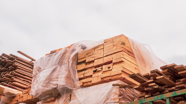 Planches de bois fraîches dans un emballage en polypropylène sur fond de ciel nuageux Pile de matériaux de construction industriels en bois naturel sur chantier