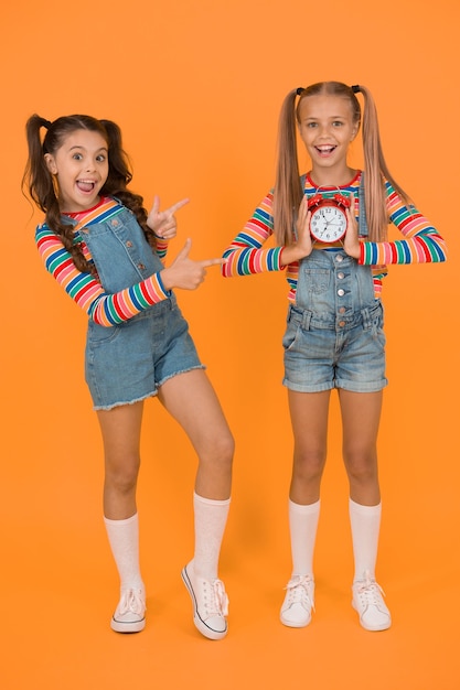 Planification et calendrier personnels. Concept de temps de comptage. Date limite. Des petites filles heureuses tiennent un réveil vintage sur fond orange. Petits enfants souriants avec horloge mécanique. Horloge scolaire.