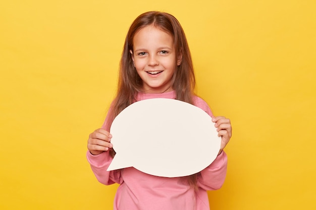 Photo planification avec un esprit clair communication avec une carte de discours petite fille joyeuse aux cheveux longs tenant une bulle de discours vide portant un sweat-shirt rose isolé sur un fond jaune