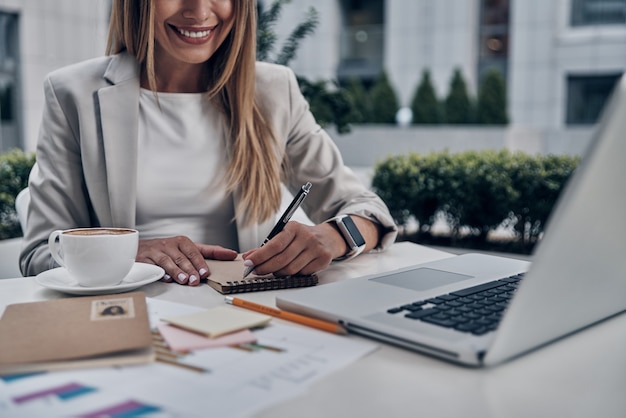 Planification de la journée. Gros plan sur une jeune femme écrivant quelque chose et souriant tout en travaillant à l'intérieur