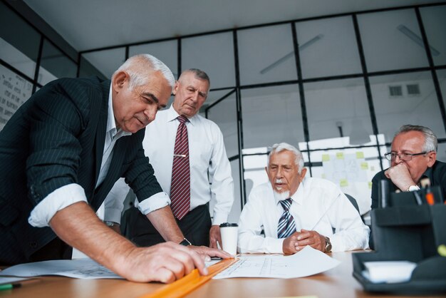 Planifier la construction en la mesurant sur papier. Une équipe âgée d'architectes d'affaires âgés a une réunion au bureau.