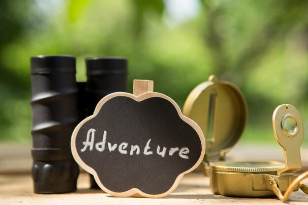 Planifiez votre concept d'aventure Aventure écrite sur un petit panneau boussole et jumelles à l'extérieur vert arrière-plan flou