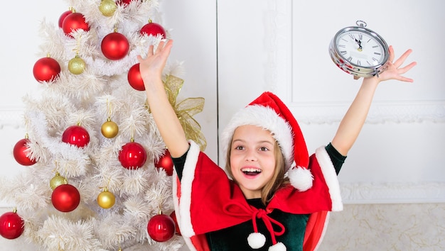 Des plans de dernière minute pour le nouvel an qui sont en fait très amusants. Dernière minute jusqu'à minuit. Compte à rebours du nouvel an. Costume de bonnet de noel fille enfant avec horloge excité visage heureux comptant le temps jusqu'au nouvel an.