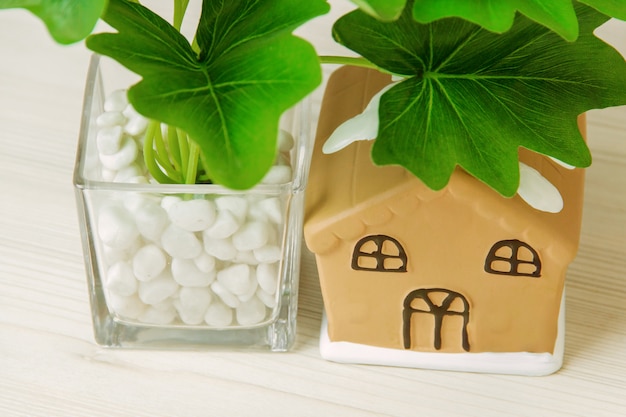 Plante d'intérieur en pot, maison de jouet sur une table en bois blanche.