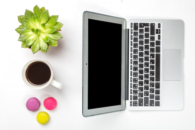 Plante verte dans un pot, une tasse de café, des macarons colorés et un ordinateur portable moderne argenté sur fond blanc