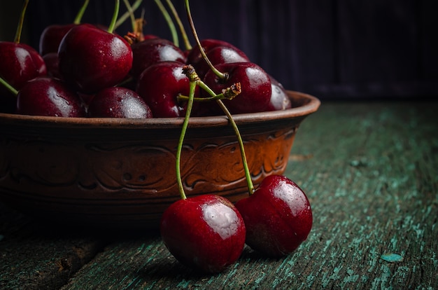 Plaque d'argile avec des cerises rouges mûres sur une vieille table en bois.