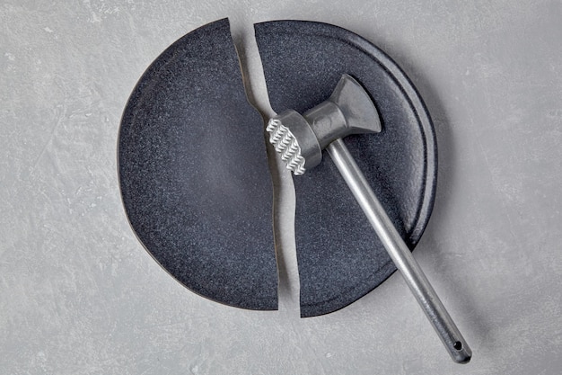 Plaque en céramique cassée et un marteau de cuisine sur une table en béton léger
