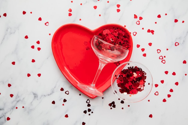 Plaque de coeur rouge de fond de dîner de saint valentin avec le verre de champagne et les confettis