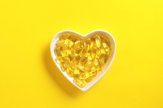 Plaque en forme de coeur avec des capsules d'huile de poisson sur fond jaune Oméga d'huile de poisson dans des capsules molles jaunes concept de santé et de beauté