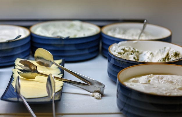 Photo plaque de fromage servie dans une assiette bleue avec des pinces en cuillère d'acier sur la table des assiettes de fête de bols de fromage à la crème savoureuse des tranches de fromage et des pinces de cuisine sur un fond de mayonnaise et de yogourt