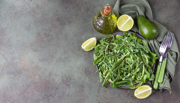 Photo plaque avec mélange vert de feuilles de salade et de microgreens, de citron vert, d'avocat et d'huile d'olive