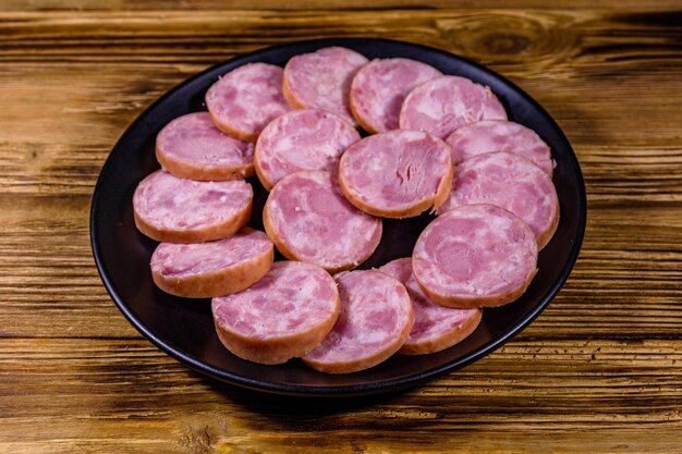 Plaque noire avec des tranches de saucisse sur une table en bois