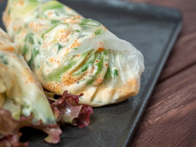 Photo sur une plaque texturée noire sont enroulés des rouleaux de printemps. un délicieux plat diététique. cuisine asiatique, gros plan