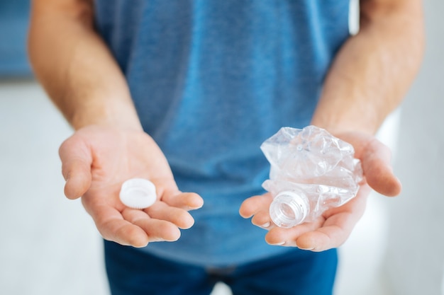 Plastique nocif. L'accent étant mis sur les mains d'un homme dans un t-shirt bleu tenant une bouteille en plastique écrasée, prête pour le recyclage