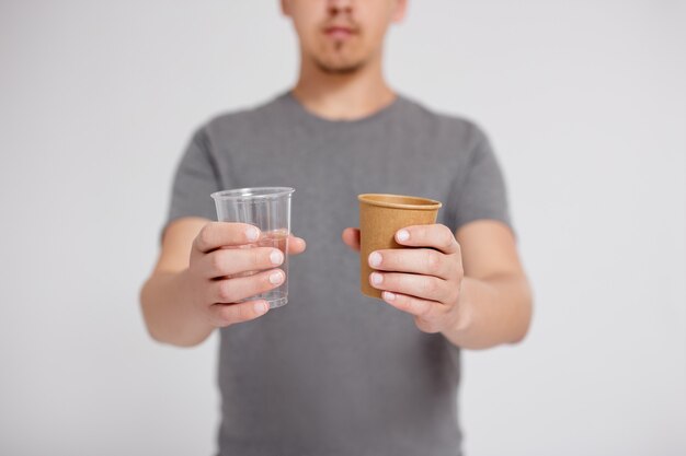 Plastique ou papier - homme choisissant entre un gobelet en plastique et un gobelet en papier écologique sur fond gris