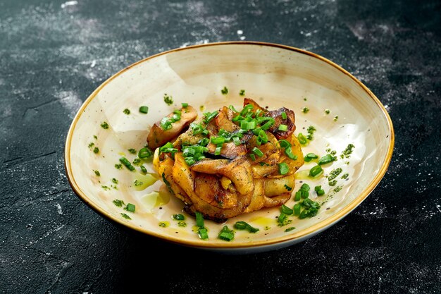 Un plat d'accompagnement appétissant - pommes de terre frites aux cèpes et oignons verts, servis dans une assiette sur une surface sombre