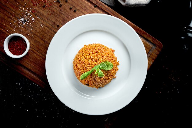 Plat d'accompagnement appétissant et sain - boulgour en sauce rouge avec des épices turques dans une assiette blanche sur une table sombre