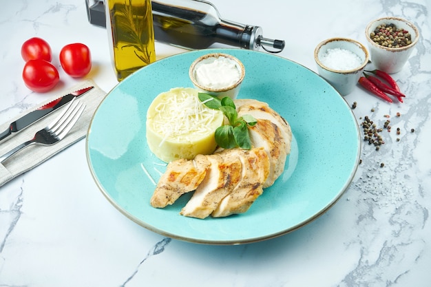 Plat appétissant et diététique - poitrine de poulet cuite au four avec sauce au fromage et purée de pommes de terre dans une assiette bleue sur une surface en marbre