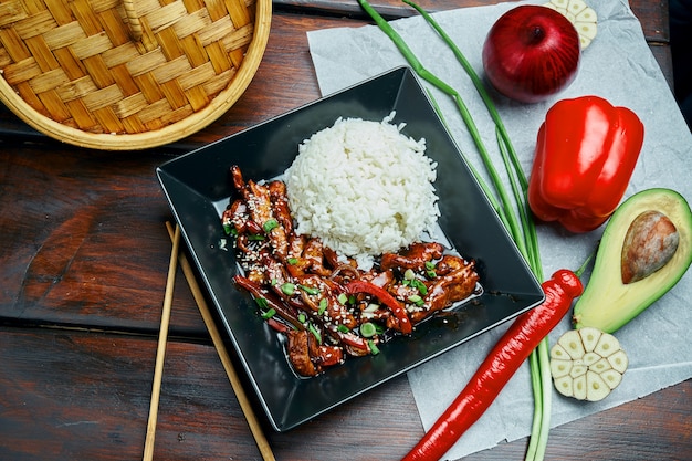 Photo un plat asiatique classique - riz avec wok de porc frit teriyaki dans une assiette noire sur une table en bois. fermer