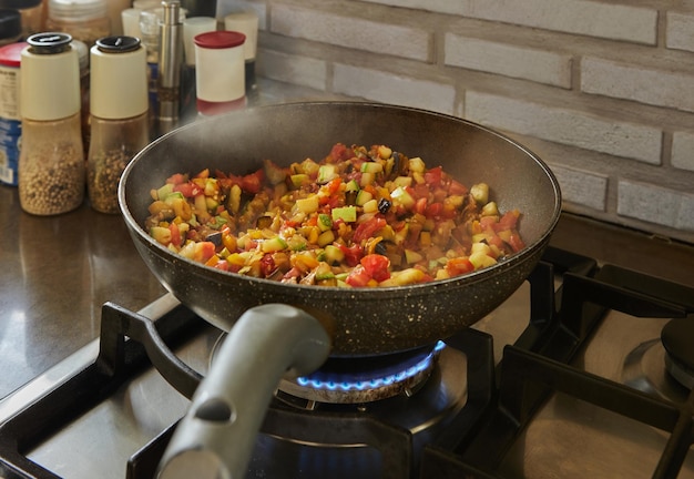 Le plat d'aubergines, de courgettes et de poivrons est frit dans une poêle sur une cuisinière à gaz