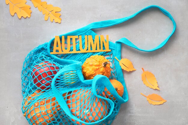 Plat à l'automne avec un sac à cordes turquoise avec des citrouilles orange, le haut vie sur pierre grise