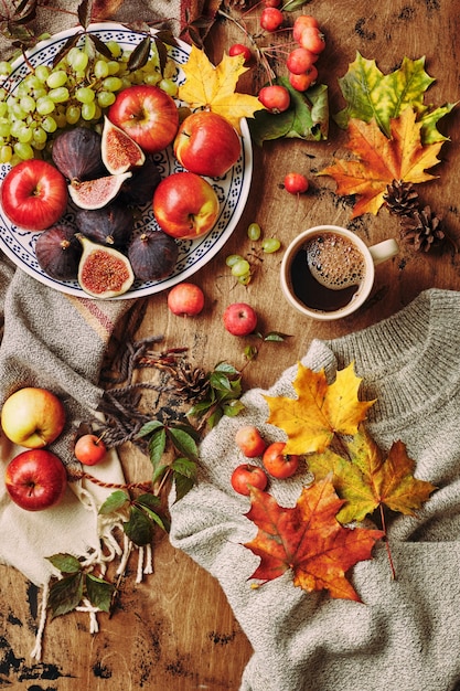 Plat aux figues pommes et raisins et tasse de café sur fond en bois avec un chandail chaud écharpe au...