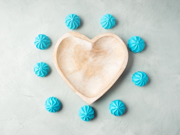 Plat en bois en forme de coeur avec des meringues douces bleues à plat