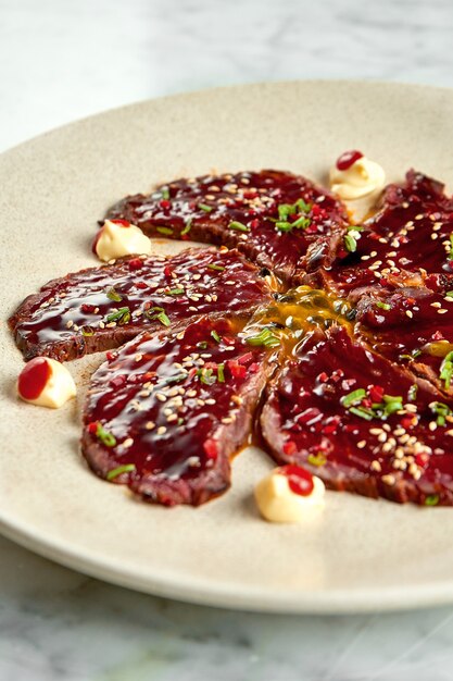 Plat classique japonais - boeuf tataki avec sauce unagi, piment, servi dans une assiette beige sur une table en marbre. Nourriture de restaurant